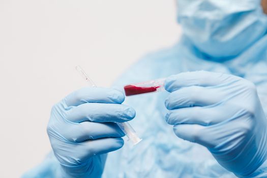 Close up of doctor hand holding blood sample. Medical equipment. Blood test. A doctor wearing personal protective equipment including mask, goggle, and suit to protect COVID 19 coronavirus infection.