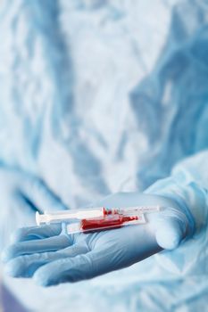 Close up of doctor hand holding syringe and blood sample. Medical equipment. Blood test. A doctor wearing personal protective equipment including mask, goggle, and suit to protect COVID 19 coronavirus infection.