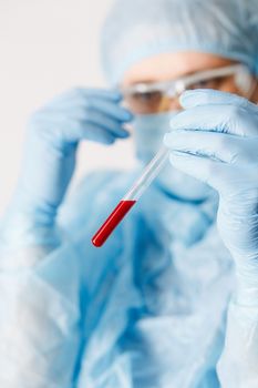 Close up of doctor hand holding blood sample. Medical equipment. Blood test. A doctor wearing personal protective equipment including mask, goggle, and suit to protect COVID 19 coronavirus infection.