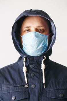 Man in hood with mask to protect him from Coronavirus. Corona virus pandemic. Young man with medical mask isolated. Person in hood with medical mask. COVID 19