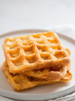 Perfect savory keto waffles. Two ingredients chaffles on plate over white marble background. Eggs and parmesan cheese low carb waffles. Extreme close up view. Vertical.