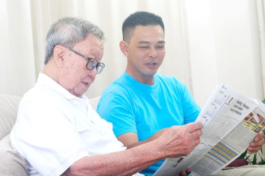 Portrait of chinese family reading newspaper together at home. Mature 80s senior man and his son