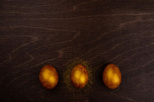 Three big golden easter eggs on dark wooden background copy space for text