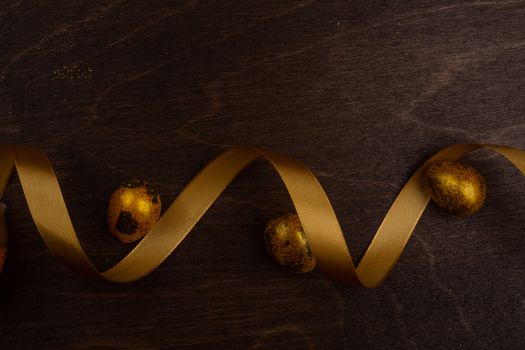 Golden luxury easter eggs and ribbon composition on dark wooden background with copy space for text card