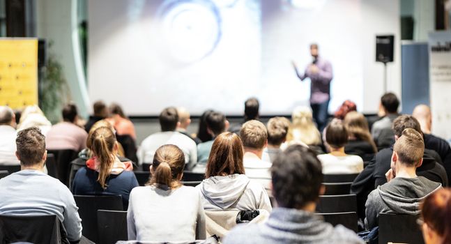 Speaker giving a talk in conference hall at business event. Rear view of unrecognizable people in audience at the conference hall. Business and entrepreneurship concept.