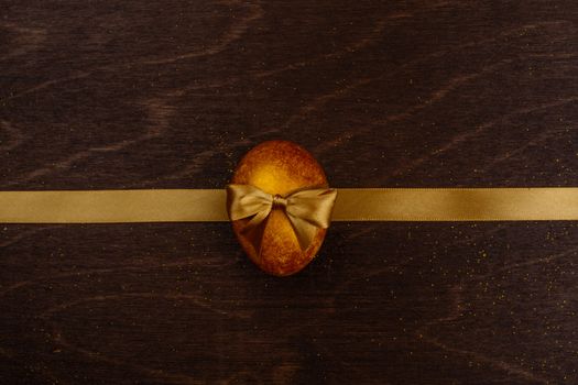 Golden luxury easter egg and ribbon composition on dark wooden background with copy space for text card