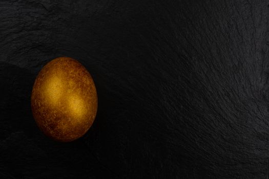 One big golden easter egg on dark black stone background copy space for text