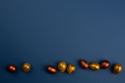 Small golden quail easter eggs in a row on blue background copy space for text