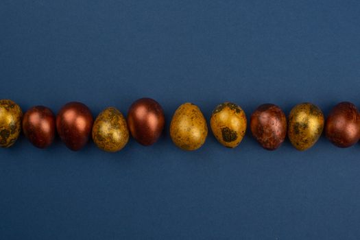 Small golden quail easter eggs in a row on blue background copy space for text