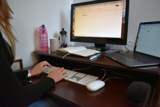 Remote working concept. A young woman typing on a keyboard at a desk in a home