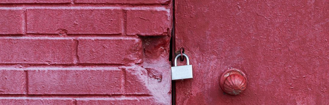 A silver padlock locks the old doors securely. Close- up view. Red brick wall. Copy space for your design
