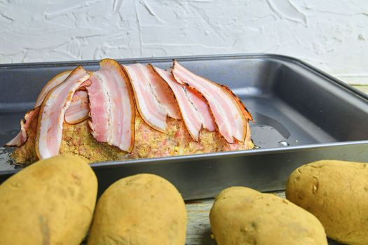 Meat loaf with slices of bacon. Home-made meat loaf on roasting pan. Potatoes foregraund