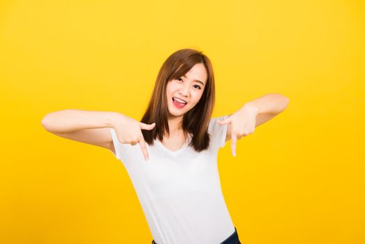 Asian happy portrait beautiful cute young woman teen standing wear t-shirt makes gesture two fingers point below down looking to camera isolated, studio shot on yellow background with copy space
