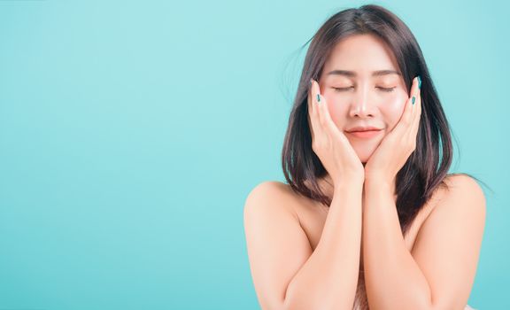 Asian happy portrait beautiful young woman standing smiling surprised excited her hands over her face and looking to camera on blue background with banner copy space for text