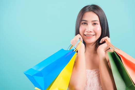 Asian happy portrait beautiful young woman standing smile in summer shopping her holding multicolor shopping bags on hand and looking to camera on blue background with copy space for text