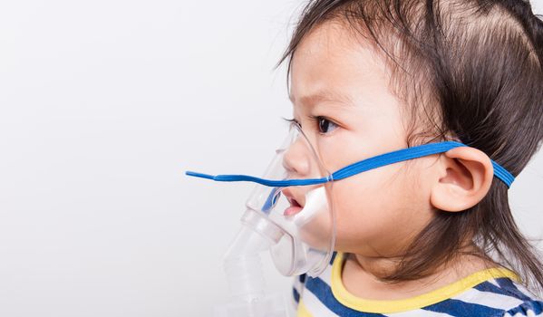 Closeup Asian face, Little baby girl sick her using steam inhaler nebulizer mask inhalation oneself on white background with copy space, health medical care