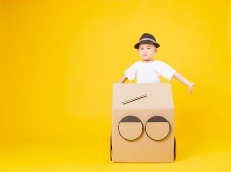 Portrait happy Asian cute little children boy smile so happy wearing white T-shirt driving car creative by cardboard, studio shot on yellow background with copy space