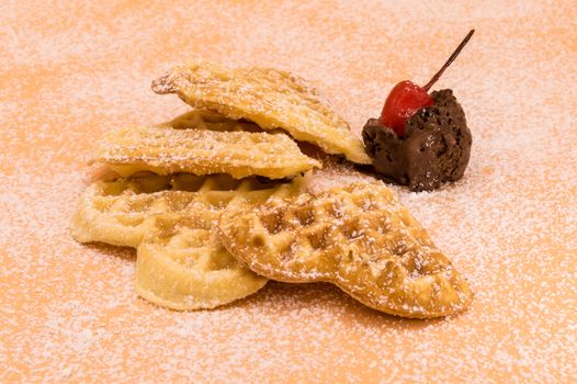 Triangle of homemade waffles with powdered sugar, a scoop of chocolate ice cream and a cherry on a pink background, isolated image of food.