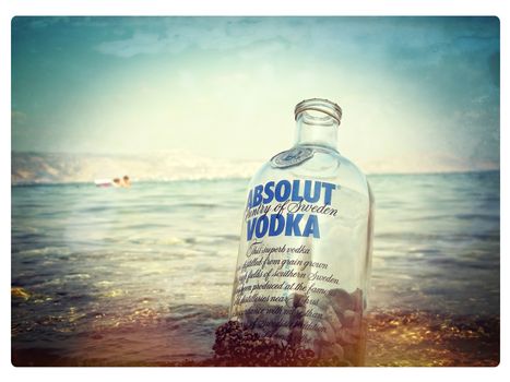 Tel Aviv, Israel - Aug 20, 2013: Empty bottle of famous Swedish Absolut Vodka filled with pebbles rocks. It lies in the seawater with blurred background. Concept of vacation, fun, and relaxation. Closeup, selective focus with copy space.