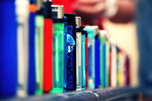 Lighters lined up. One blue color lighter stands out from the rest. Man's face Illustrated on it and it looks like he glances out to the camera. Closeup, selective focus with copy space.