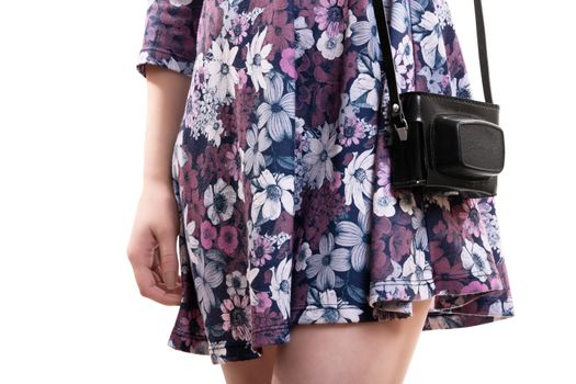 Close up of the mid section of a girl in flowery dress carrying a vintage camera in a leader camera bag, isolated on white background.