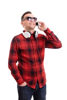 Communication and technology concept. Portrait of a handsome smiling young man in plaid shirt talking on his mobile phone and wearing headphones around his neck, isolated on a white background.