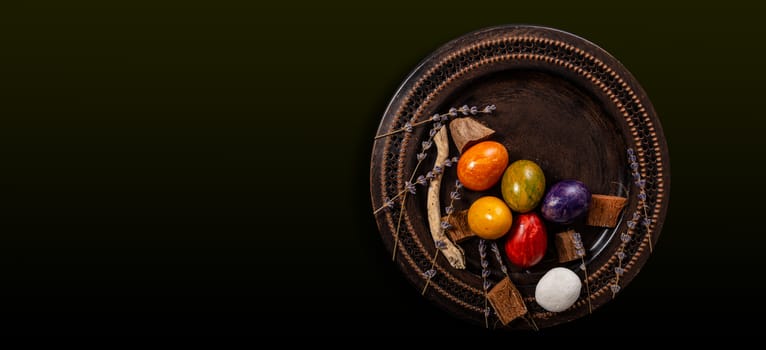 Colored easter Eggs in a plate with black background and copy space. With grass and flowers