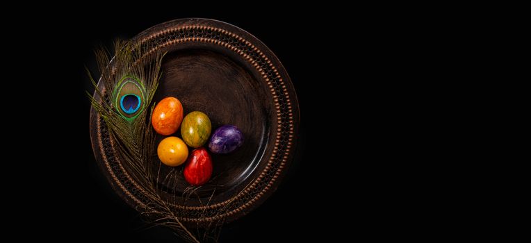 Colored easter Eggs in a plate with black background and copy space. With grass and flowers