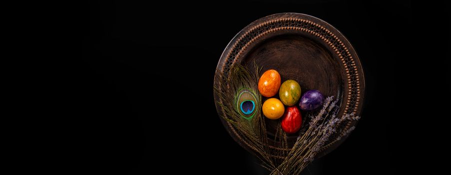 Colored easter Eggs in a plate with black background and copy space. With grass and flowers