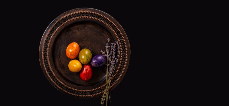 Colored easter Eggs in a plate with black background and copy space. With grass and flowers