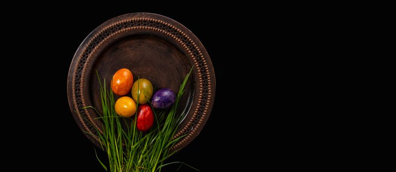 Colored easter Eggs in a plate with black background and copy space. With grass and flowers