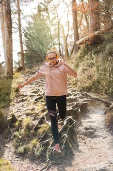 Active sporty woman running in autumn fall forest jumping over the roots on the path. Healthy lifestyle image of young active caucasian woman jogging outside in nature.