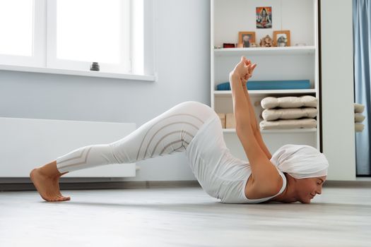 Pretty young woman in sportswear sitting on studio floor in difficult position while doing yoga