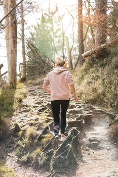 Rear view of active sporty woman listening to the music while running in autumn fall forest. Female runner training outdoor. Healthy lifestyle image of young caucasian woman jogging outside.