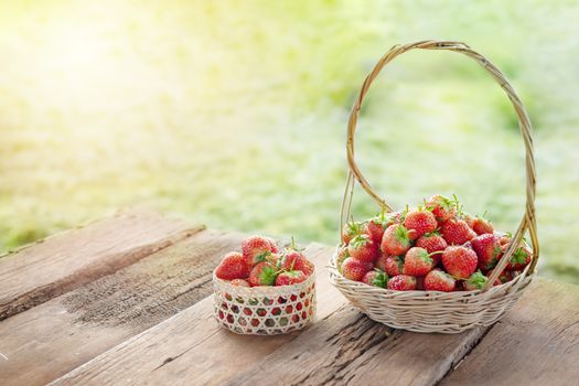 fresh ripe strawberries in basket over wooden floor with green field background