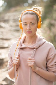 Portrait of beautiful sports woman with hoodie and headphones during outdoors training session. Healthy lifestyle image of young caucasian woman jogging outside.