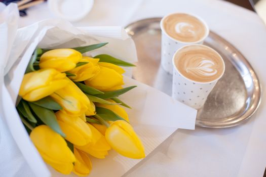 Yellow tulips bouquet with coffee cups over wooden table