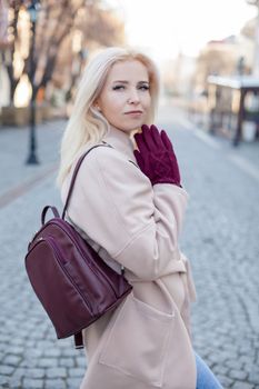 Outdoor of gorgeous woman with blond hair in elegant coat and gloves walking in street