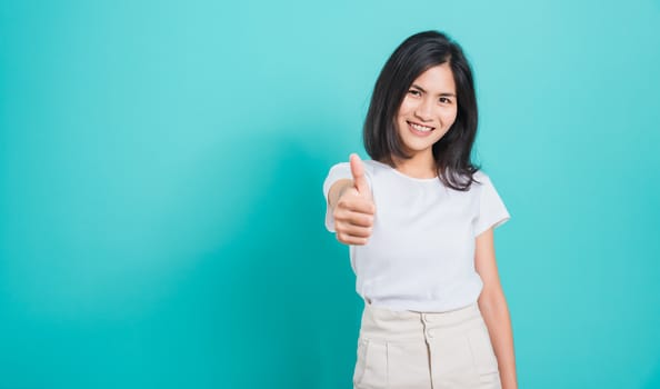 Portrait Asian beautiful young woman standing, She made finger thumbs up, Ok sign to agree and looking at camera, shoot photo in studio on blue background, There was copy space