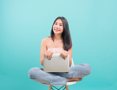Asian happy portrait beautiful young woman sitting on chair smile her  holding laptop computer and looking to camera on blue background with copy space for text
