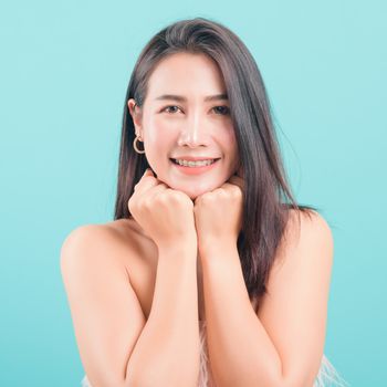 Asian happy portrait beautiful young woman standing smiling surprised excited her keeps hands pressed together under the chin and looking to camera on blue background with copy space for text