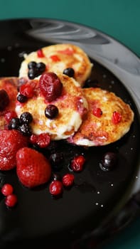 Cheese Pancakes with berries on a black plate. Vertical photo