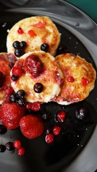Cheese Pancakes with berries on a black plate. Vertical photo