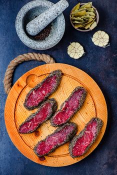 Stone mortar bowl with pestle, garlic, bay leaf and wooden cutting board with raw pepper steaks on stone surface