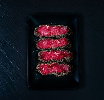 Pepper steaks on black stone plate top view