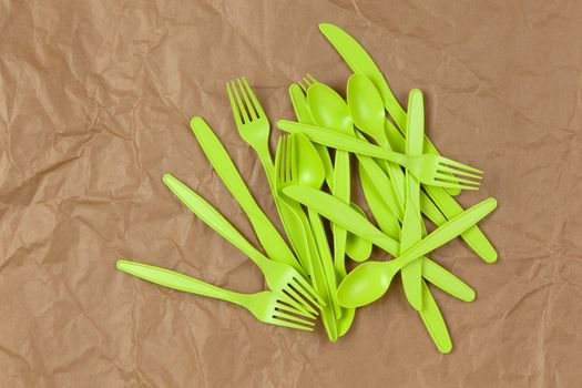 Biodegradable reusable recyclable green forks, spoons, knifes made from corn starch on brown crumpled craft paper. Eco, zero waste, alternative to plastic concept. Flat lay. Horizontal. Close-up.