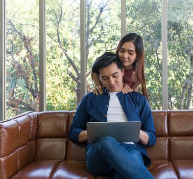 Young lovers spend time together on holidays in the living room. Both of them are interested in internet product information while the man held laptop computer.