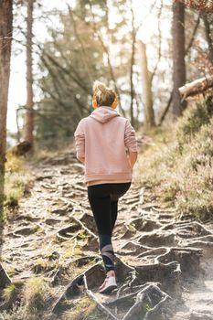 Rear view of active sporty woman listening to the music while running in autumn fall forest. Female runner training outdoor. Healthy lifestyle image of young caucasian woman jogging outside.