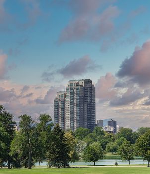 A modern high rise condominium building rising into sky beyond a green park