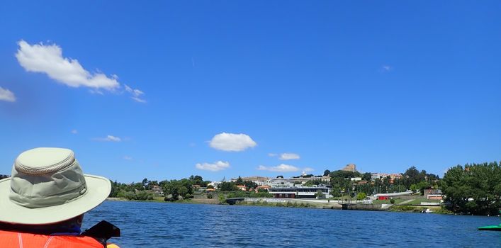 person in kayak with hat on river looking at city on shore